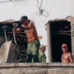 Três trabalhadores atuam na reforma de um edifício em um canteiro de obras.