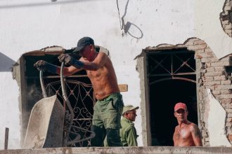 Três trabalhadores atuam na reforma de um edifício em um canteiro de obras.