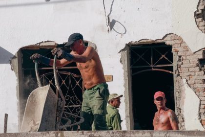 Três trabalhadores atuam na reforma de um edifício em um canteiro de obras.