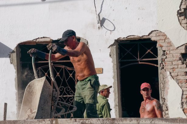 Três trabalhadores atuam na reforma de um edifício em um canteiro de obras.