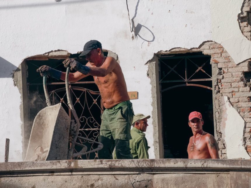 Três trabalhadores atuam na reforma de um edifício em um canteiro de obras.