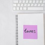 Notebook com a anotação “taxes” ao lado de um teclado, representando documentos e sistemas fiscais.