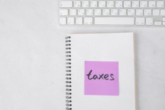 Notebook com a anotação “taxes” ao lado de um teclado, representando documentos e sistemas fiscais.