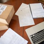 Documentos, laptop e caixas organizados sobre uma mesa de trabalho de um pequeno negócio.