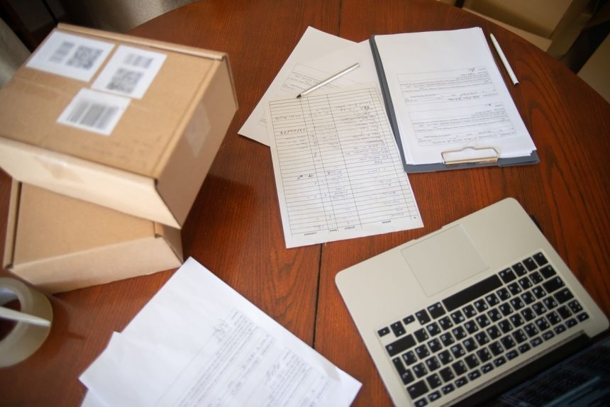Documentos, laptop e caixas organizados sobre uma mesa de trabalho de um pequeno negócio.