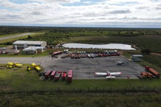 Vista aérea de uma base de combate a incêndios com aviões, caminhões e equipes de emergência mobilizadas.