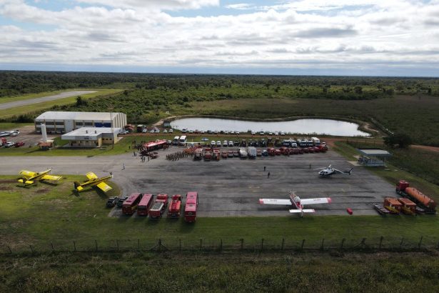 Vista aérea de uma base de combate a incêndios com aviões, caminhões e equipes de emergência mobilizadas.