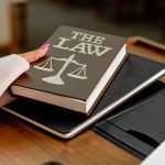 Livro sobre direito e balança da justiça sobre uma mesa de madeira.