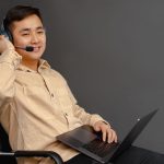 Agente de atendimento sorrindo, usando headset e laptop em ambiente interno